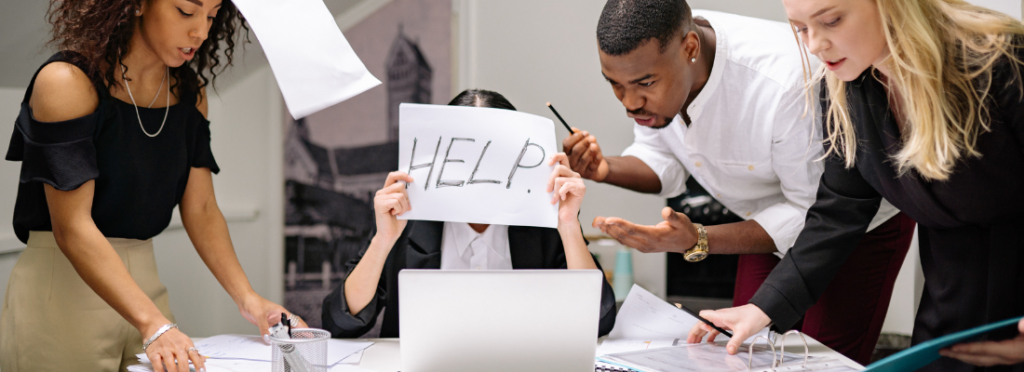 Pessoa em ambiente corporativo cercada por colegas enquanto segura uma folha com a palavra “HELP”, representando pressão psicológica e medo de denunciar no trabalho